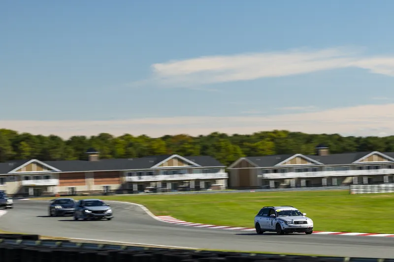 Audi A4 Avant #6 leading a group of cars past trackside buildings